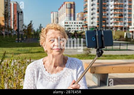 Femme aînée détendue assise sur un banc et fait selfie avec smartphone Banque D'Images
