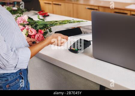 Main d'une femme avec smartphone faisant le paiement sans contact au fleuriste. Banque D'Images