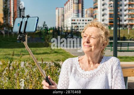 Femme aînée détendue assise sur un banc et fait selfie avec smartphone Banque D'Images