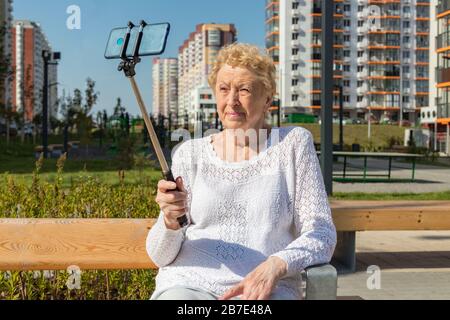 Femme aînée détendue assise sur un banc et fait selfie avec smartphone Banque D'Images