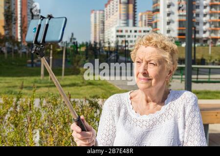 Femme aînée détendue assise sur un banc et fait selfie avec smartphone Banque D'Images