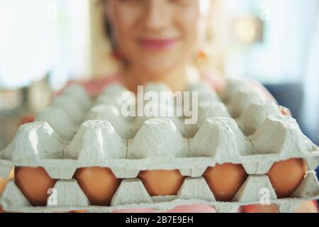 Gros plan sur la femme souriante dans le salon en journée ensoleillée de printemps montrant la grande boîte de carton d'œufs. Banque D'Images