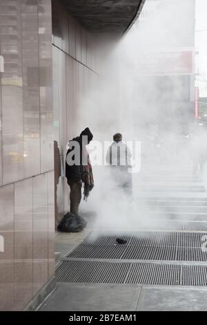 Les sans-abri se réchauffent dans la vapeur qui s'est produite par des grilles sur le trottoir le long de la 8ème avenue par Madison Square Garden un matin d'hiver. NEW YORK. Banque D'Images