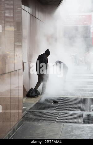 Les sans-abri se réchauffent dans la vapeur qui s'est produite par des grilles sur le trottoir le long de la 8ème avenue par Madison Square Garden un matin d'hiver. NEW YORK. Banque D'Images