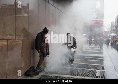 Les sans-abri se réchauffent dans la vapeur qui s'est produite par des grilles sur le trottoir le long de la 8ème avenue par Madison Square Garden un matin d'hiver. NEW YORK. Banque D'Images