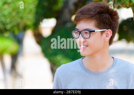 Asiatique beau adolescent portant des lunettes, Portrait jeune homme hipster gai sourire avec un visage heureux au parc sur fond vert nature en thaï Banque D'Images