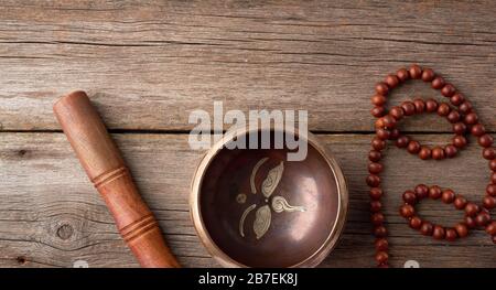 Bol en cuivre chantant tibétain avec un clapper en bois et un rosaire de prière sur une table en bois gris, gros plan Banque D'Images