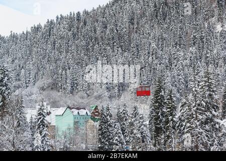 Téléphérique rouge en bas de la montagne jusqu'au village. Vue de dessus du bâtiment dans la forêt de sapins enneigée. Hiver froid jour Banque D'Images