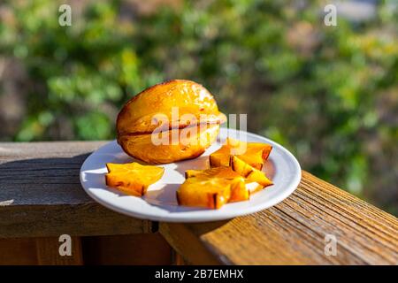 Macro gros plan de starfruit jaune d'orange tranché sur plaque sur la barrière de la rampe de pont à l'extérieur avec des couleurs vives Banque D'Images