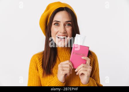 Image de la belle femme adulte brunette portant un chapeau de béret souriant et tenant des billets de voyage isolés sur fond blanc Banque D'Images