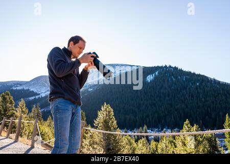 Laissez-passer l'automne avec un photographe homme et un appareil photo dans la forêt nationale de White River, au Colorado, avec des pins verts et des sommets enneigés Banque D'Images