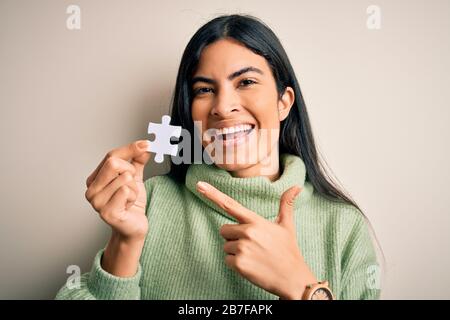 Jeune femme hispanique qui tient la pièce de puzzle comme solution de coopération sur les affaires très heureux pointant avec la main et le doigt Banque D'Images