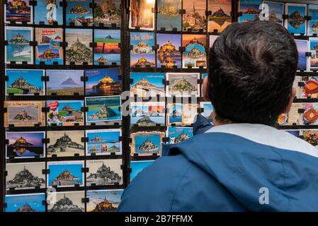 Homme regardant les cartes postales du Mont Saint-Michel exposées dans une boutique de souvenirs Banque D'Images