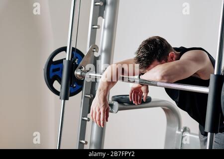 Jeune bodybuilder fatigué penchant sur le barbell après avoir levé de lourds poids dans la salle de gym Banque D'Images