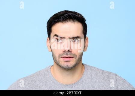 Un jeune homme curieux et attentif, avec des sourcils relevés isolés sur un fond bleu clair Banque D'Images