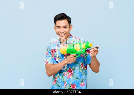 Homme asiatique souriant jouant avec un pistolet à eau isolé sur fond bleu studio pour le festival Songkran en Thaïlande et en Asie du Sud-est Banque D'Images