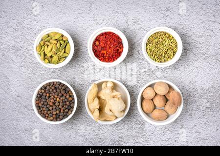 Mélange d'épices aromatiques coriandre, poivre noir, bergamote, gingembre séché, noix de muscade, paprika en tasses blanches sur fond de béton gris vue dessus plat le mettre Banque D'Images