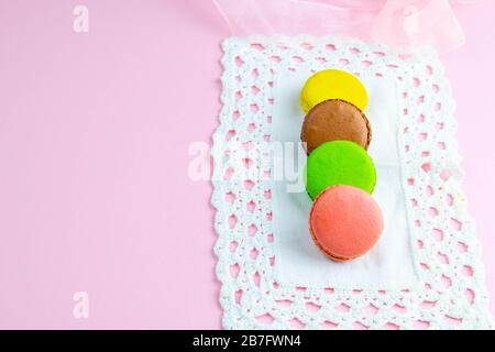 Plusieurs macarons multicolores aux couleurs pastel sur une serviette blanche sur fond rose Banque D'Images