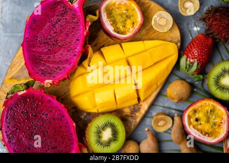 Assortiment de fruits exotiques tropicaux biologiques. Arrière-plan gris. Plat de composition estivale. Vue de dessus, gros plan de fruits frais en tranches sur Banque D'Images