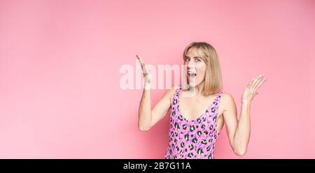 Surprise superbe femme blonde dans un maillot de bain rose léopard avec une large bouche ouverte regardant l'appareil photo, souriant sur un fond rose Banque D'Images