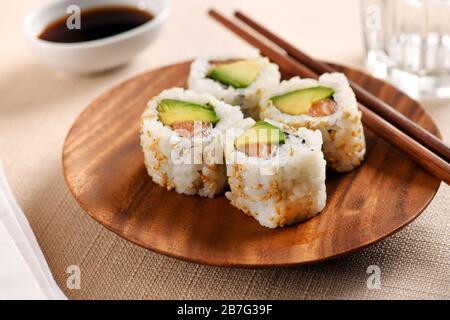 Quatre rouleaux de sushis uramaki traditionnels avec du saumon frais cru, de la poire avocat, du nori et du riz sur un plateau circulaire en bois avec des baguettes servies à la table sur un l Banque D'Images