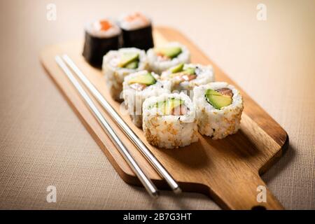 Plateau en bois avec service de sushi uraki avec poire d'avocat frais, saumon, riz, nori et graines de sésame, ainsi qu'une paire de baguettes avec f sélectif Banque D'Images