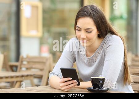 Une jeune femme sérieuse qui vérifie son smartphone sur une terrasse de café Banque D'Images