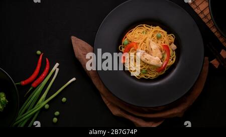 Vue de dessus des nouilles Schezwan ou Chow Mein avec légumes et poulet en plaque noire sur table noire Banque D'Images