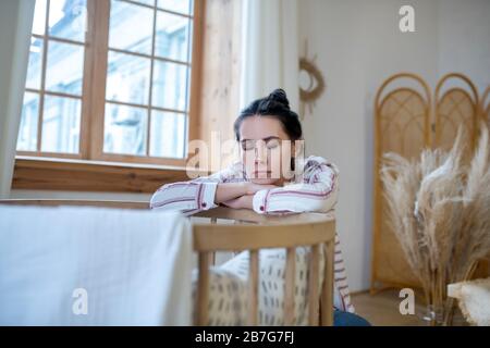 Maman fatiguée assise au lit, reposant sa tête sur les mains, les yeux fermés Banque D'Images