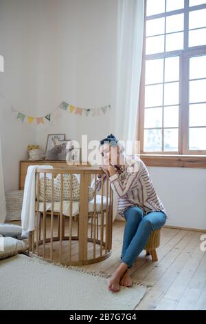 Maman fatiguée assise au lit avec des yeux fermés, reposant sa tête sur les mains Banque D'Images