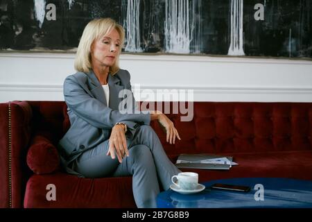 Vue grand angle sur une femme d'affaires moderne mûre regardant de manière pensive tout en étant assise sur un canapé en velours dans un café, espace de copie Banque D'Images