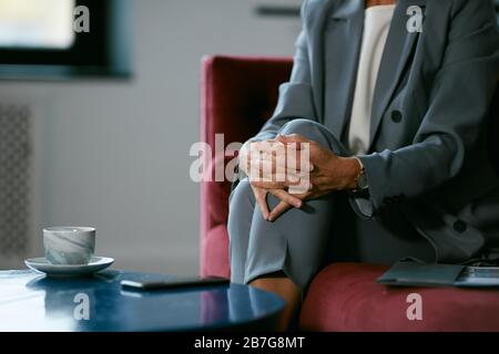 Gros plan sur une femme d'affaires non reconnaissable qui attend dans un café, se concentrer sur les mains claquées au-dessus du genou et de la tasse à café, espace de copie Banque D'Images