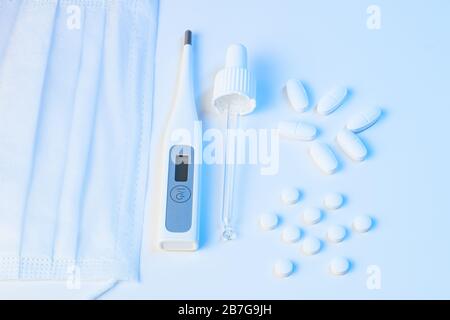 thermomètre électronique, masque de protection, pilules pour pipettes et comprimés se trouvent sur un fond blanc avec un éclairage bleu Banque D'Images