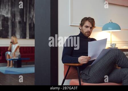 Portrait de l'homme barbu à la main tenant des documents tout en étant assis dans un élégant café intérieur avec une femme en arrière-plan, espace de copie Banque D'Images