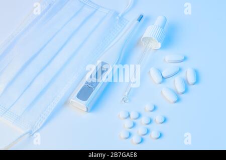 thermomètre électronique, masque de protection, pilules pour pipettes et comprimés se trouvent sur un fond blanc avec un éclairage bleu Banque D'Images