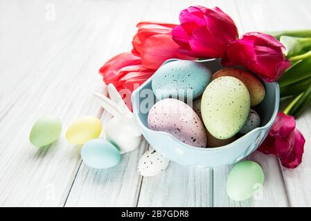 Fond de Pâques avec œufs colorés dans un bol et tulipes roses sur fond blanc en bois. Vue de dessus avec espace de copie Banque D'Images