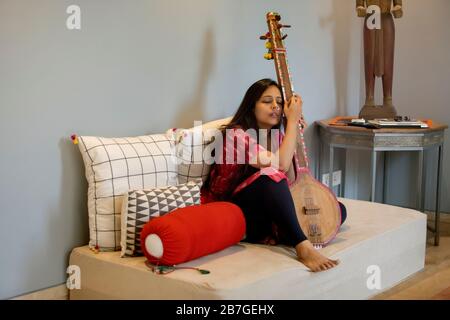 Femme assise dans son salon jouant de la musique sur son tambourra. Banque D'Images