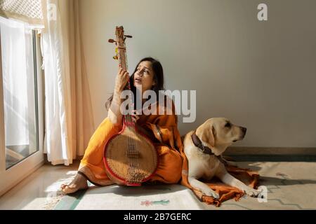 Femme assise avec son chien à côté d'elle et jouant de la musique sur son tambourra et chantant. Banque D'Images