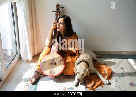 Femme assise avec son chien à côté d'elle et jouant de la musique sur son tambourra et chantant. Banque D'Images