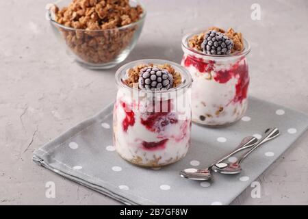 Muesli au miel croustillant de granola avec des mûres surgelées, du fromage cottage et du yaourt naturel, un délicieux petit déjeuner sain, situé dans des pots en verre sur un Banque D'Images