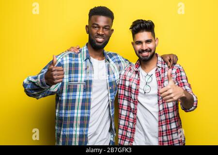 Portrait de deux jeunes hommes heureux montrant des pouces vers le haut sur fond jaune Banque D'Images