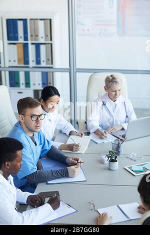 Vue en grand angle du groupe de médecins assis à table ronde pendant le conseil médical ou la conférence en clinique, espace de copie Banque D'Images