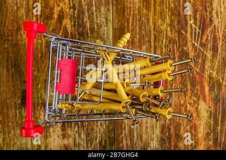 Tas de chevilles en plastique avec vis métalliques se trouvent dans le tas dans le panier miniature. Concept d'achat de réparations à domicile. Vue de dessus. Gros plan. Banque D'Images