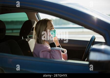 Femme dans un masque de protection conduisant une voiture sur la route. Transport en toute sécurité. Banque D'Images