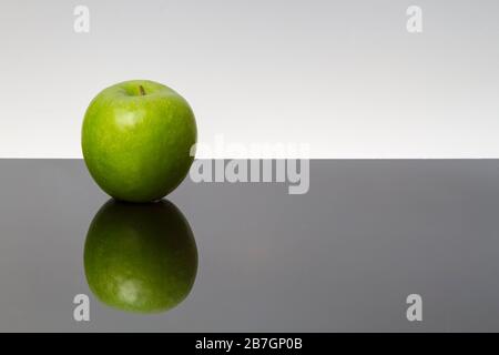 Pommes vertes avec gouttes d'eau sur la table réfléchissante, isolées sur fond sombre.espace de copie. Banque D'Images