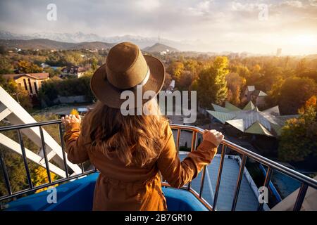 Femme avec chapeau à la cabine de la grande roue dans le parc de l'automne au coucher du soleil Banque D'Images