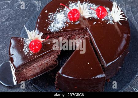 Gâteau au chocolat de forêt noire avec tarte aux cerises remplie de glaçage au chocolat noir sur le dessus décoré de cerises en conserve, une tranche placée sur un gâteau Banque D'Images