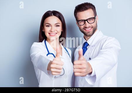 Des travailleurs médiques heureux. Portrait de deux médecins en manteaux et verres blancs montrant le pouce vers le haut sur fond blanc Banque D'Images
