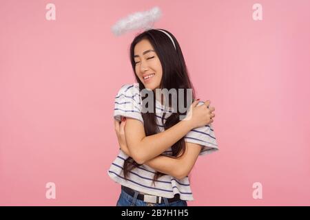 Portrait d'une étonnante fille angélique avec de longs cheveux brunette et halo sur la tête souriant contently et se serpentant, concept d'amour de soi, soutien. In Banque D'Images