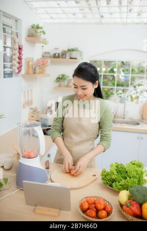 Image de jeune dame debout dans la cuisine using tablet computer et la cuisson de légumes grillés Banque D'Images